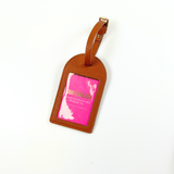 Brown self-finishing needlepoint luggage tag with textured exterior, adjustable strap, and clear rectangular window for personalized stitching.