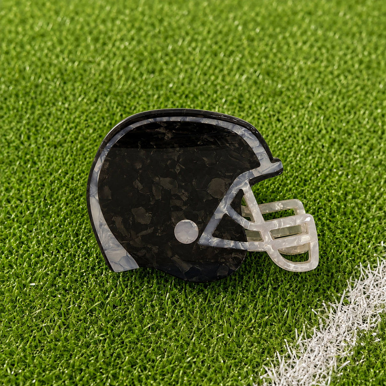 A black football helmet shaped claw clip on green turf background
