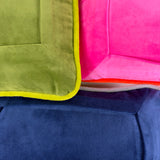 Close-up of colorful velvet needlepoint pillows featuring soft velvet fabric, contrasting piping, and shades of pink, green, and navy blue.