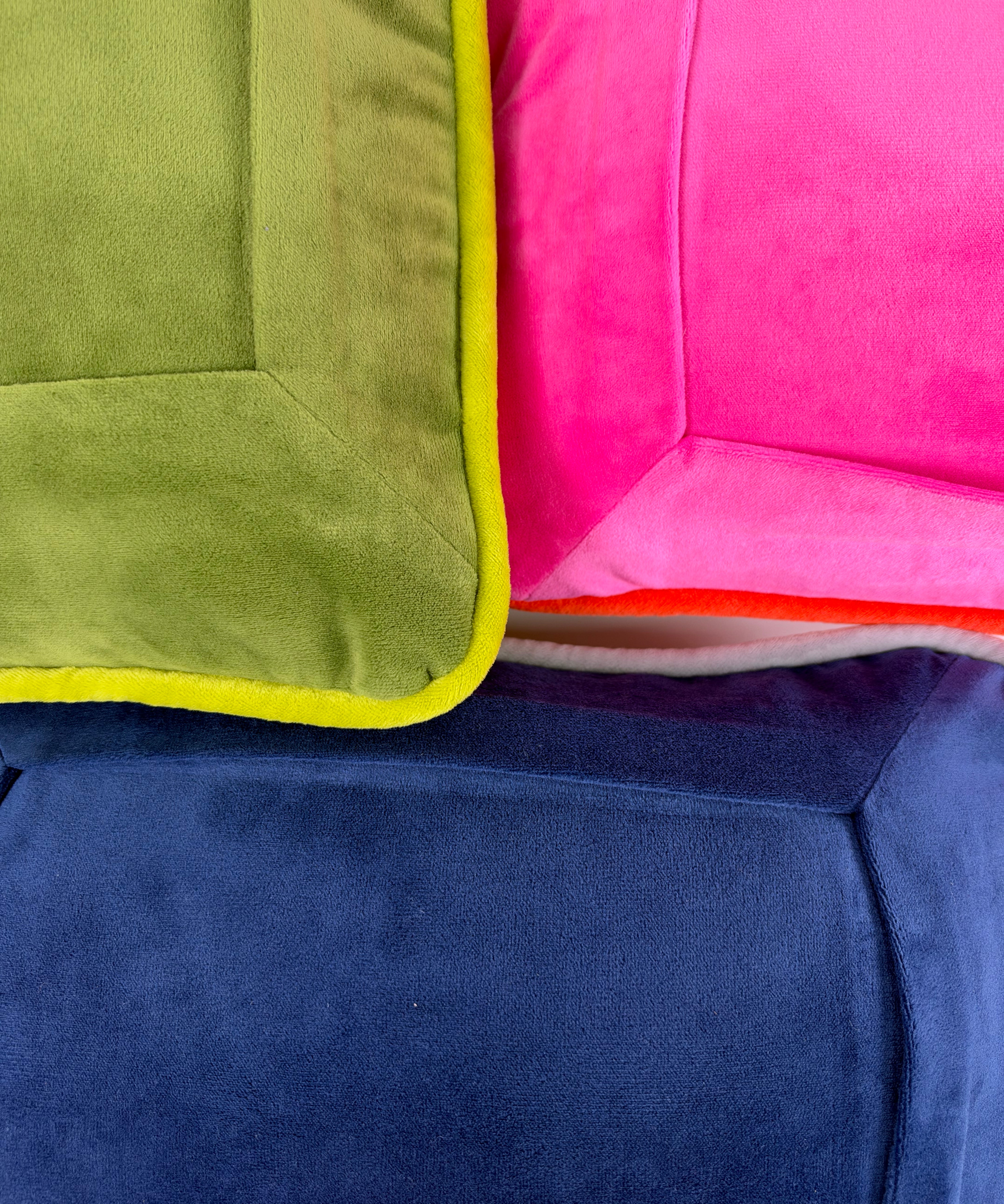 Close-up of colorful velvet needlepoint pillows featuring soft velvet fabric, contrasting piping, and shades of pink, green, and navy blue.