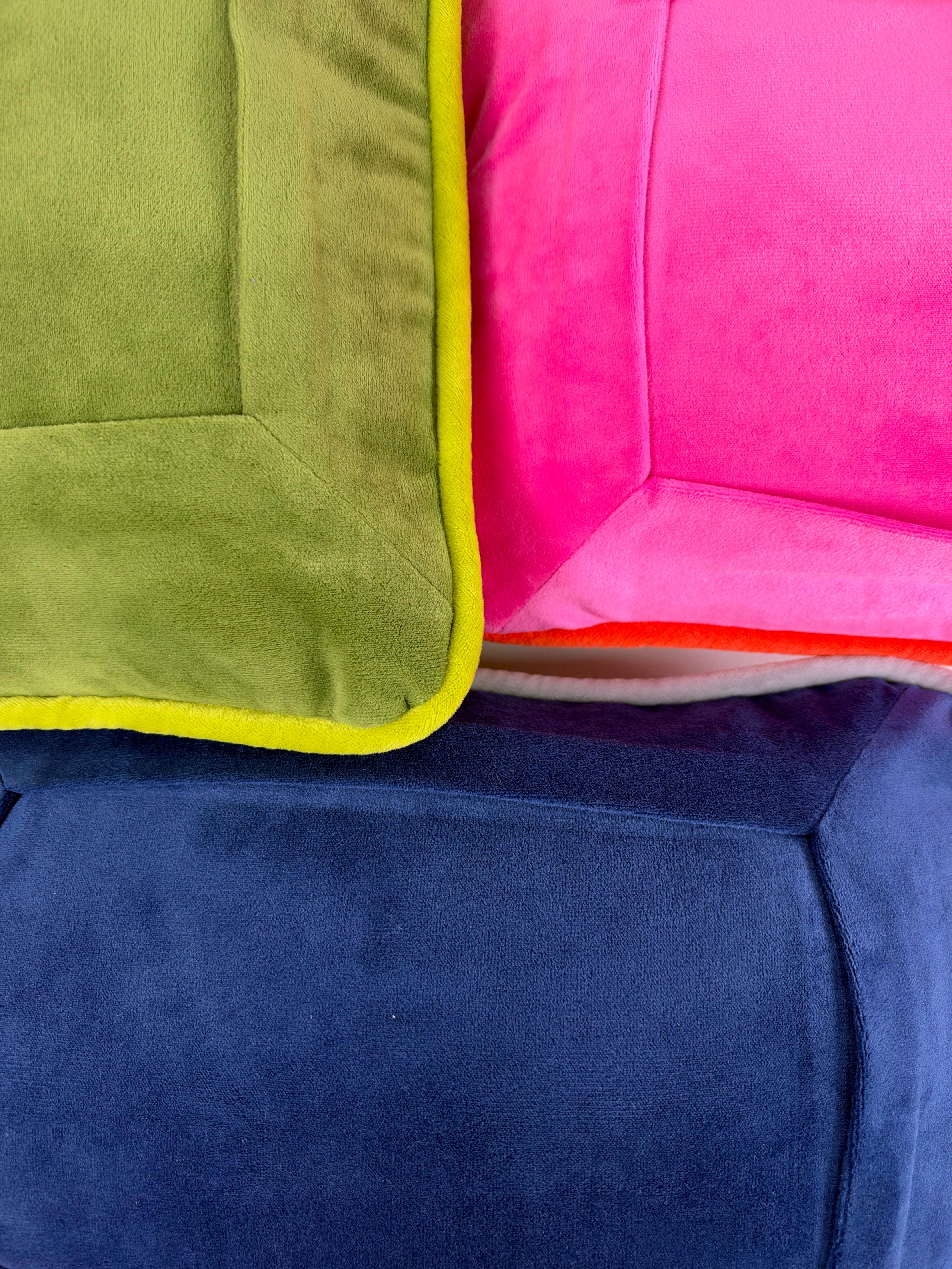 Close-up of colorful velvet needlepoint pillows featuring soft velvet fabric, contrasting piping, and shades of pink, green, and navy blue.