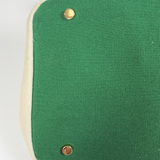 Close-up of green bottom panel with protective gold metal feet and cream canvas trim on the Parker needlepoint tote.