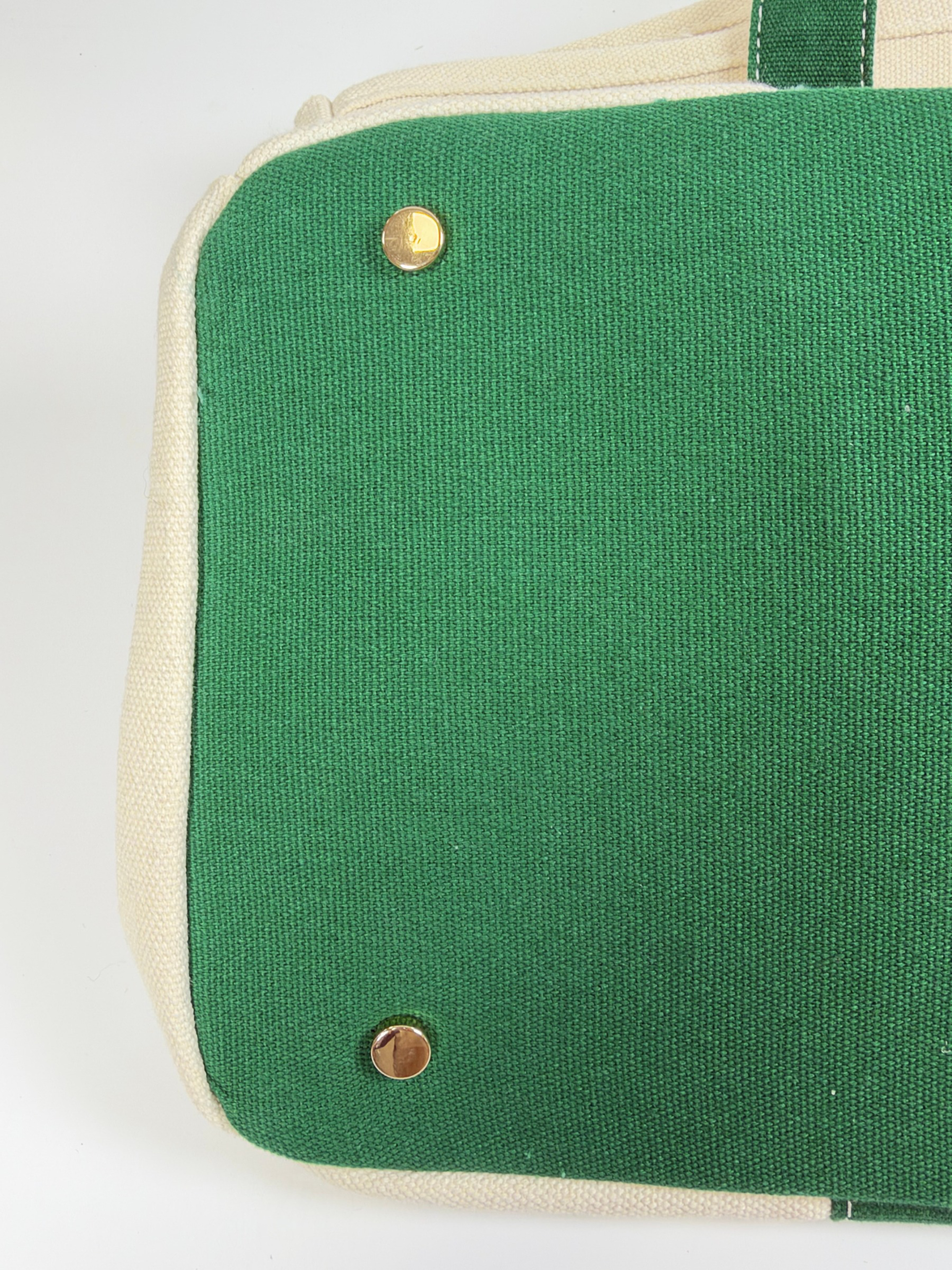 Close-up of green bottom panel with protective gold metal feet and cream canvas trim on the Parker needlepoint tote.