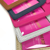 Close-up of Duo Threads self-finishing needlepoint luggage tags in brown, navy, pink, silver, and gold with textured exteriors and clear insert windows.