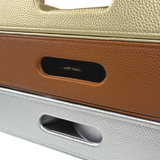 Close-up of stacked self-finishing needlepoint trays in metallic gold, brown, and silver, featuring textured exteriors and built-in cutout handles.