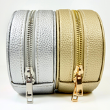 Round self-finishing needlepoint travel jewelry cases in metallic gold and silver featuring textured exteriors and coordinating zippered closures.