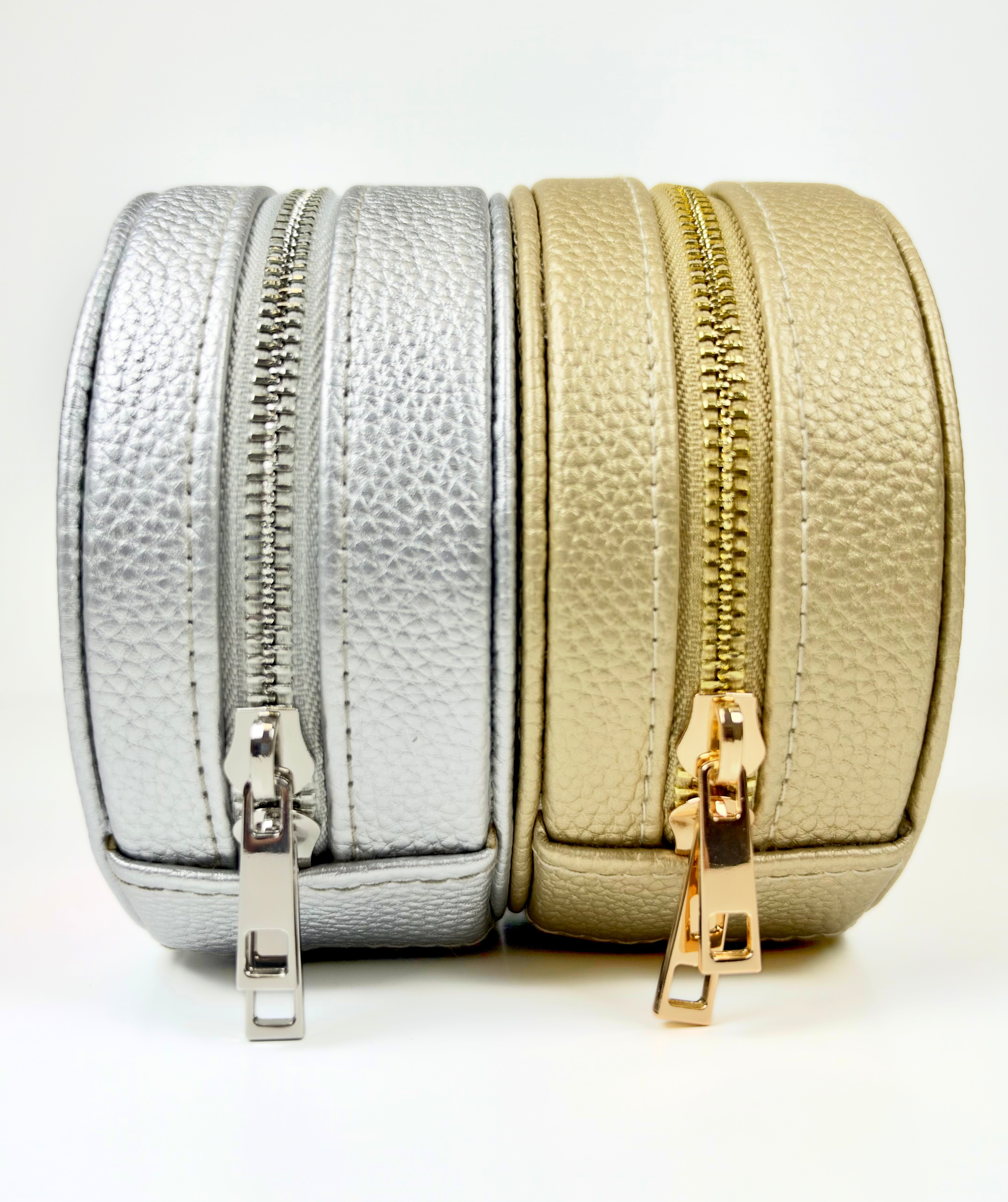 Round self-finishing needlepoint travel jewelry cases in metallic gold and silver featuring textured exteriors and coordinating zippered closures.