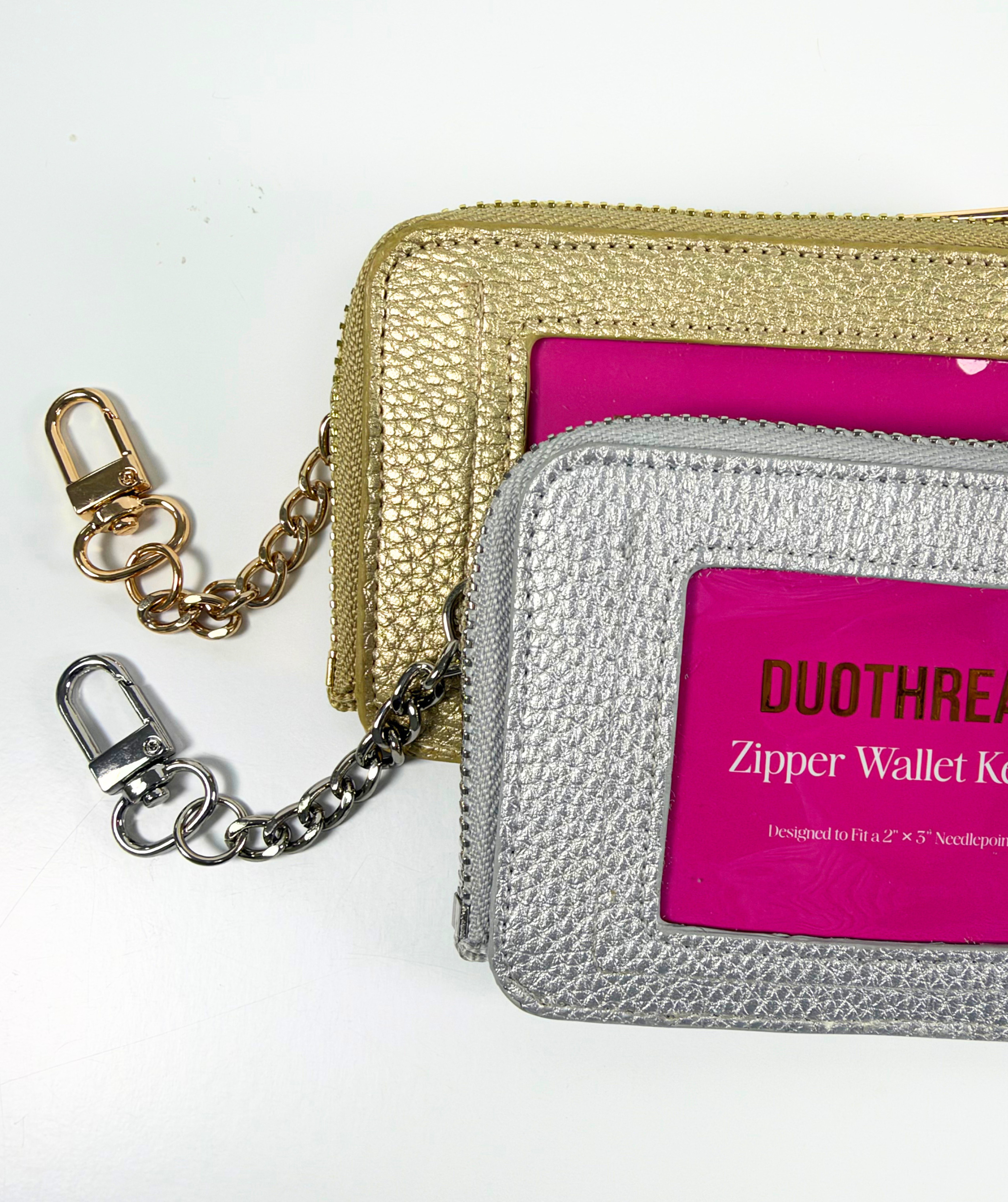 Close-up of gold and silver On-the-Go self-finishing needlepoint wallets featuring textured metallic exteriors, zippered closures, and coordinating clip-on chains.