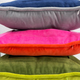 Stacked velvet needlepoint decorative pillows in navy, gray, hot pink, orange, olive green, and lime green with coordinating piped edges.