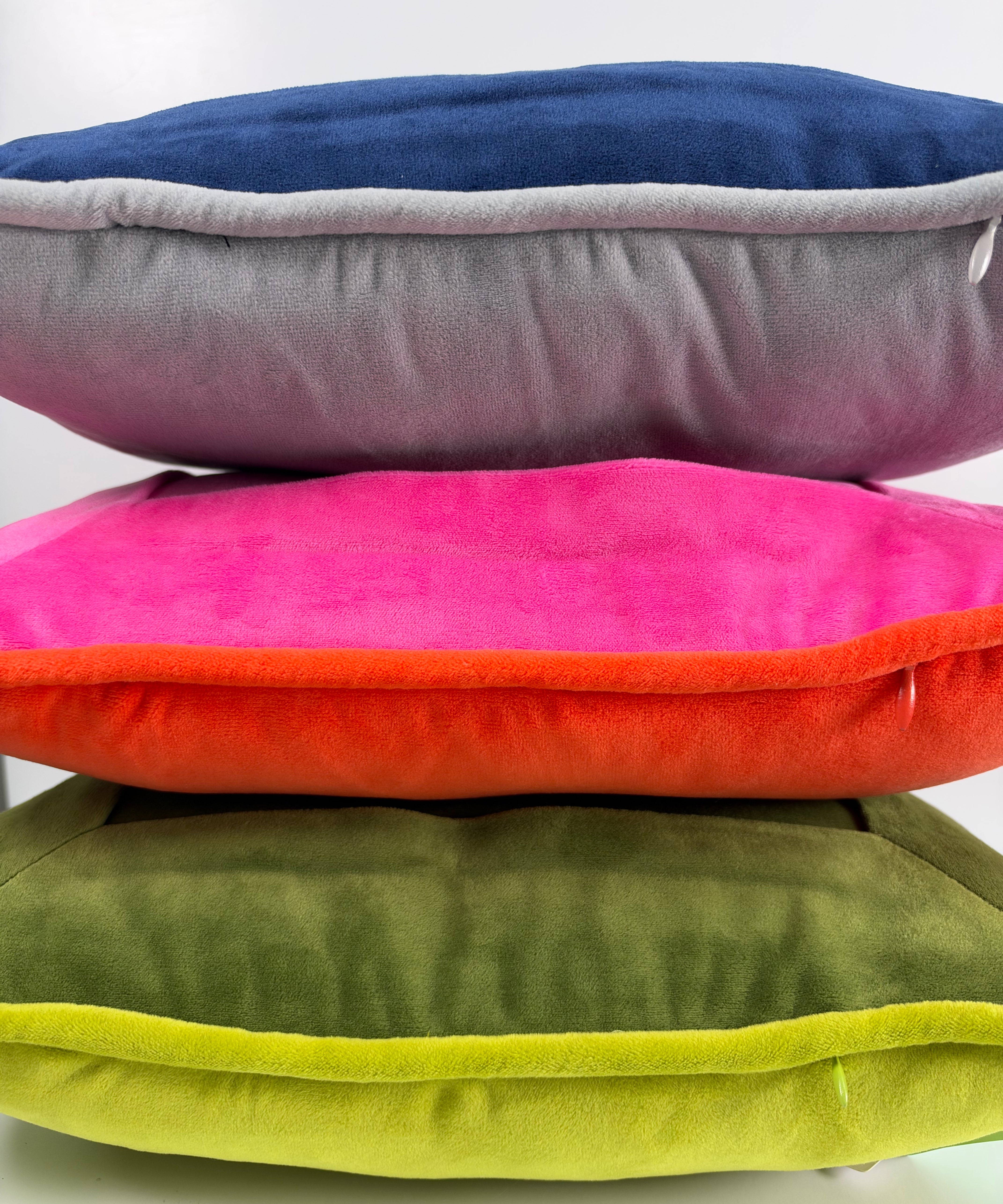 Stacked velvet needlepoint decorative pillows in navy, gray, hot pink, orange, olive green, and lime green with coordinating piped edges.