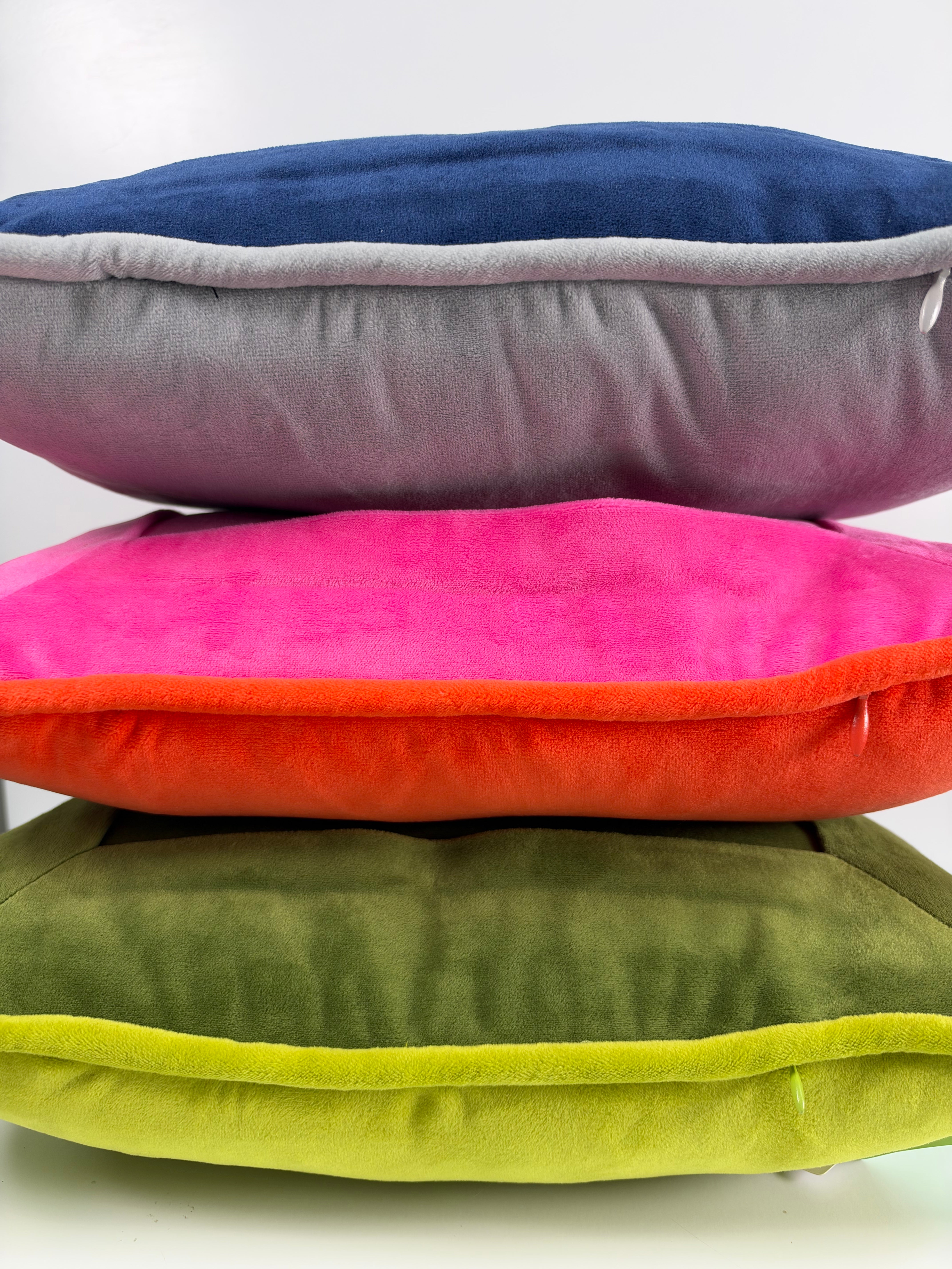 Stacked velvet needlepoint decorative pillows in navy, gray, hot pink, orange, olive green, and lime green with coordinating piped edges.