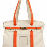 Parker self-finishing needlepoint boat tote bag with bright orange straps, cream canvas exterior, gold hardware, and front insert.