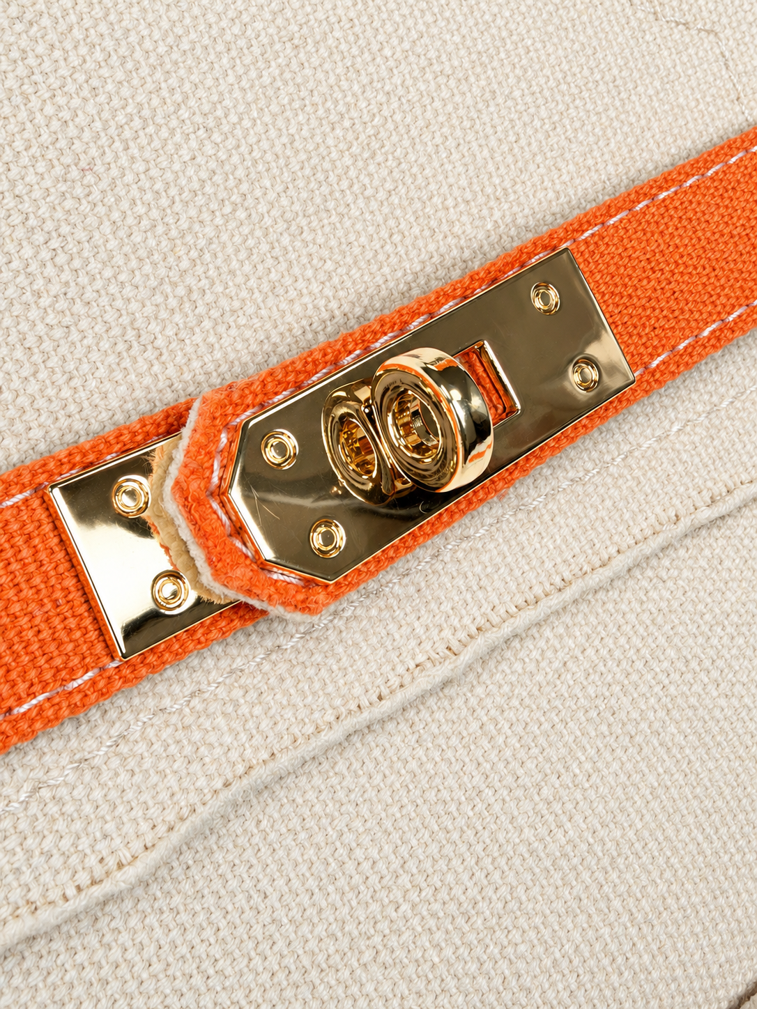 Close-up of gold-tone turn-lock buckle detail on the Parker needlepoint tote with vibrant orange trim and cream canvas.