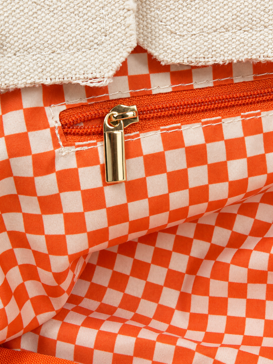 Close-up of the Parker needlepoint tote's interior zippered pocket with gold-tone zipper and orange and white gingham lining.