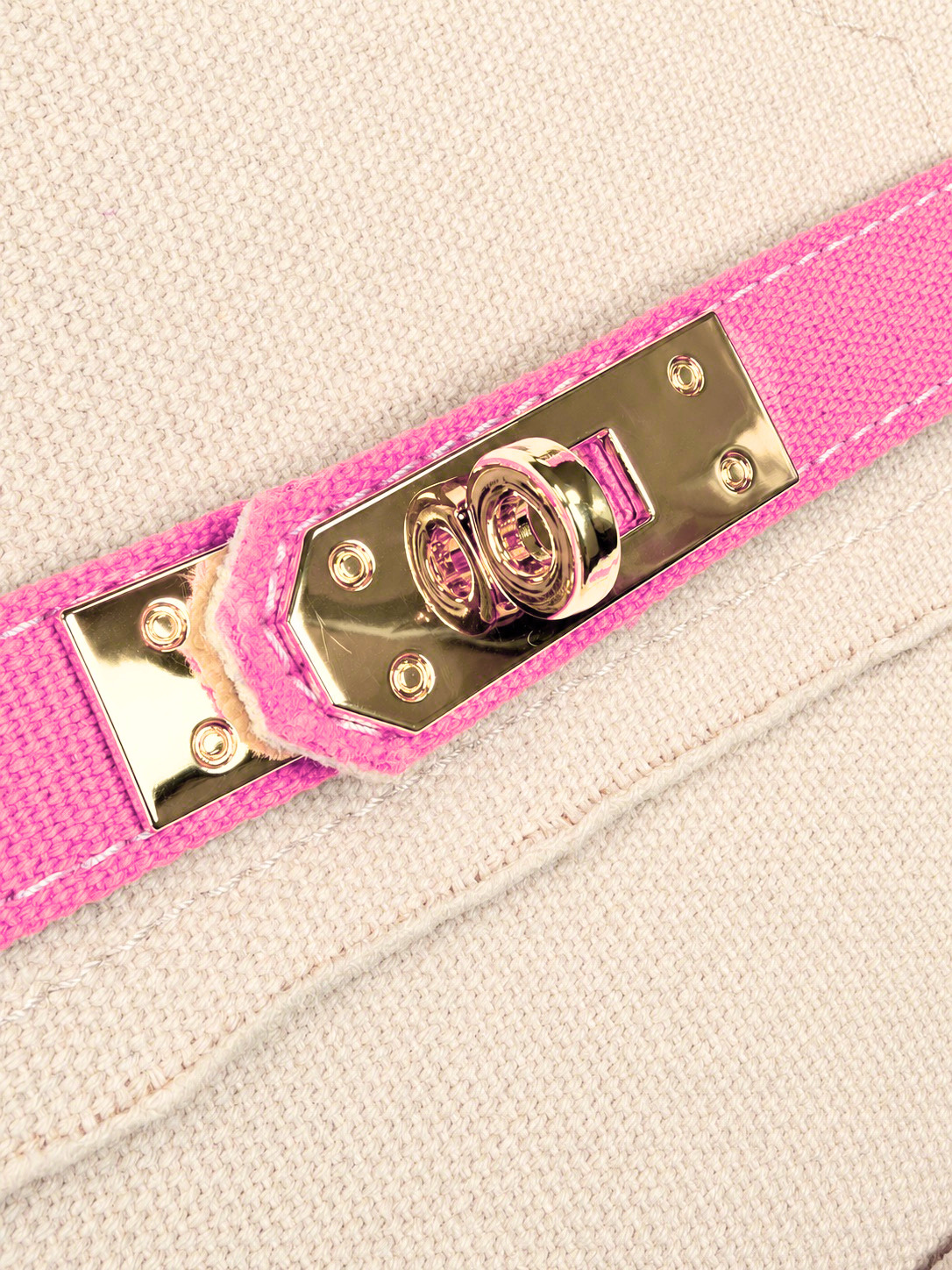 Close-up of polished gold-tone turn-lock hardware on the Parker needlepoint tote with bright pink trim and cream canvas exterior.