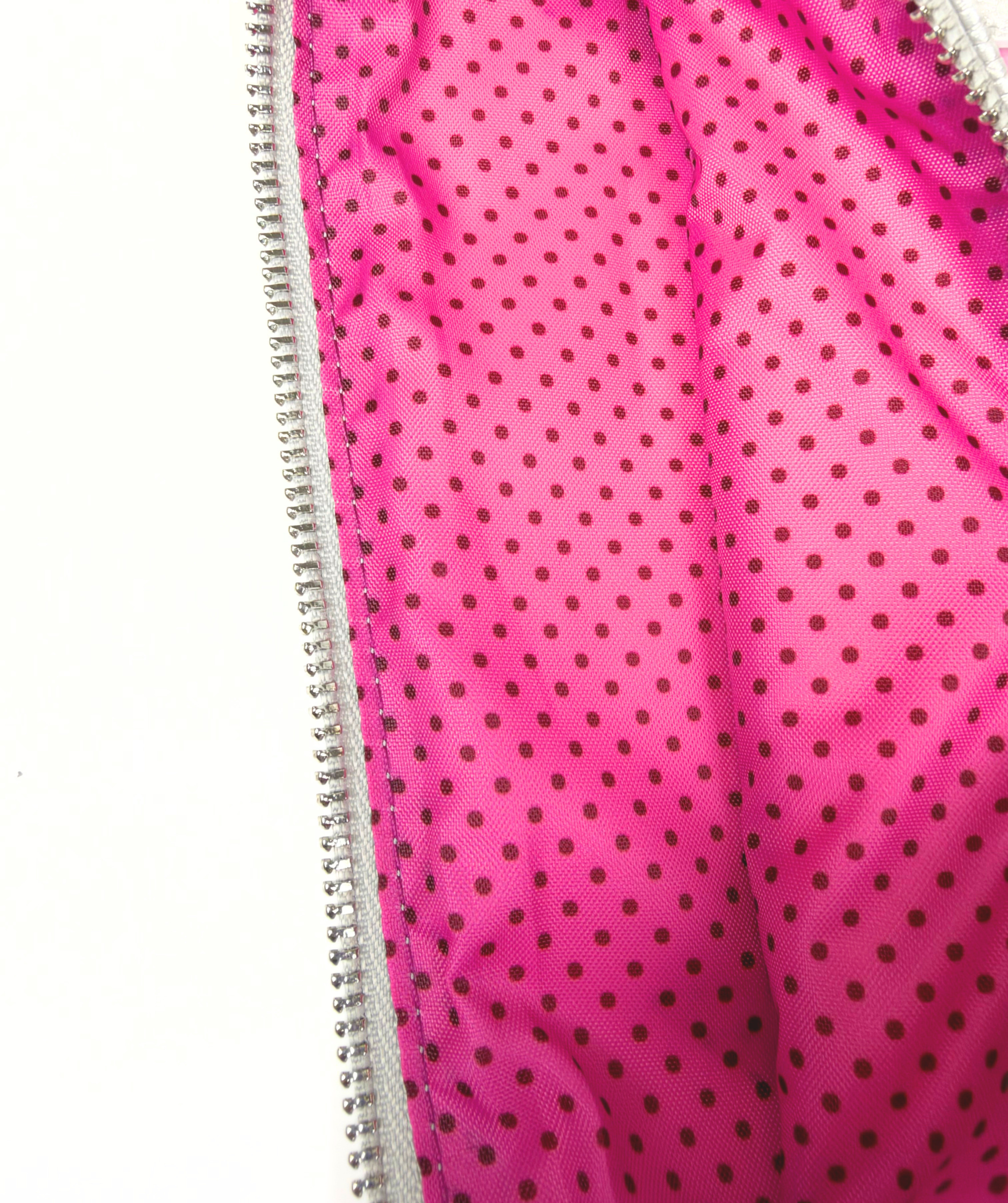 Close-up of the needlepoint travel case's bright pink interior lining with a playful black polka dot pattern and zippered opening.