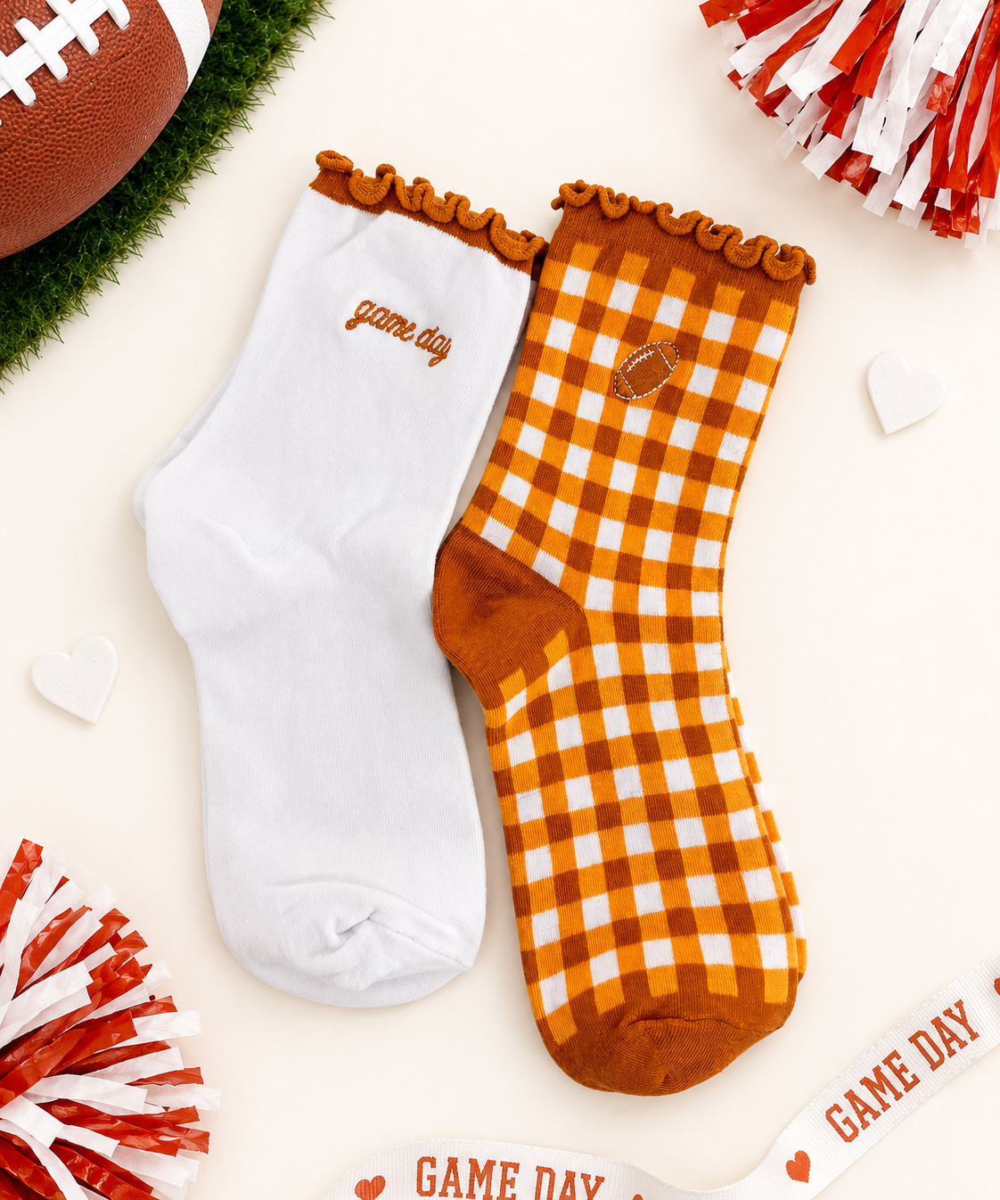 Two decorative ankle socks displayed on a light cream background with football-themed props. One sock is solid white with 'game day' embroidered in brown near the cuff.