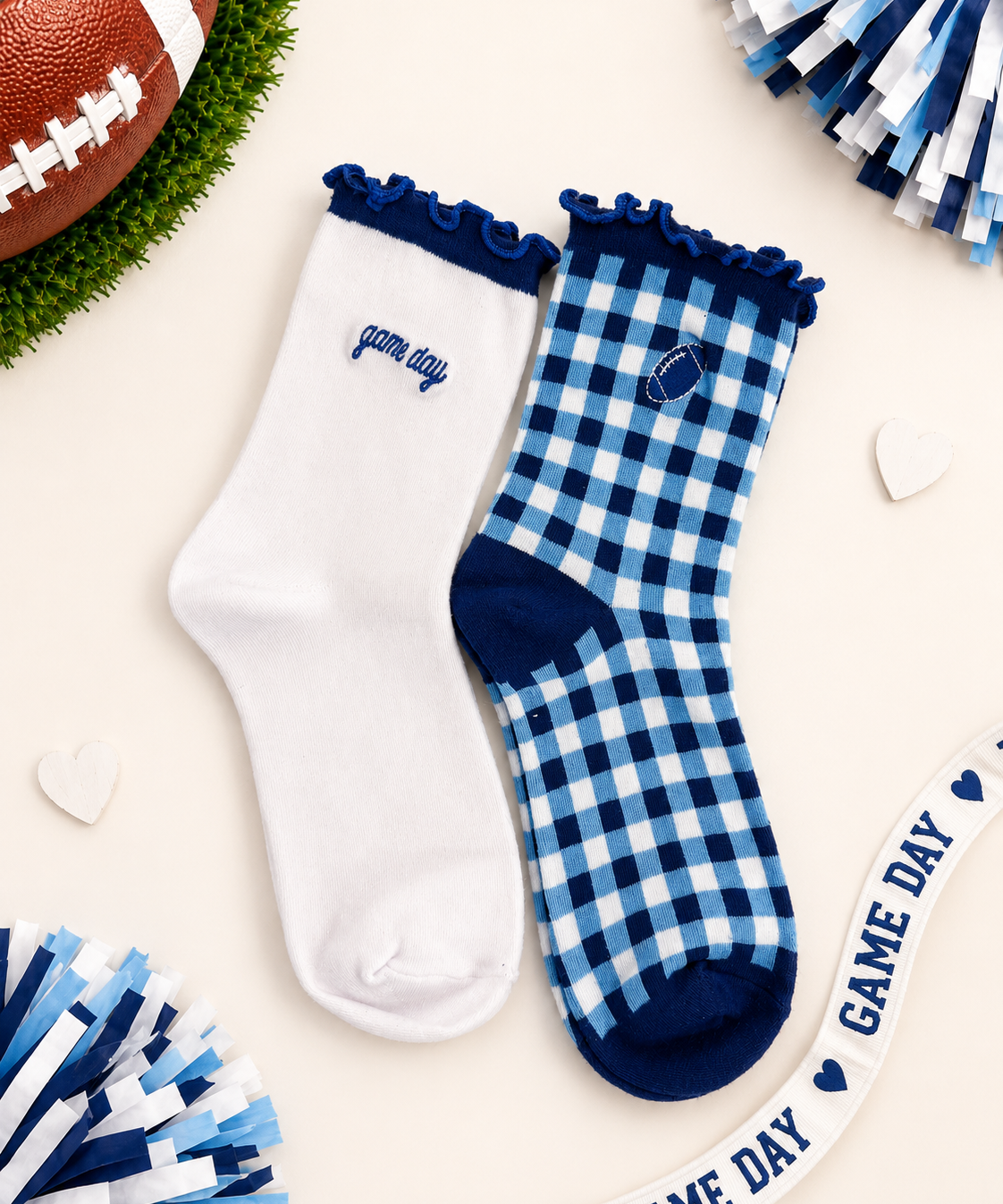 Two pairs of women's crew socks styled in a flat-lay arrangement. One pair is solid white with a navy blue ruffled cuff and 'game day' text on the side.