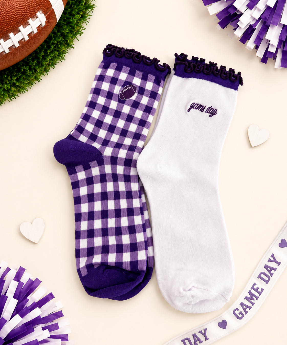 Two decorative ankle socks displayed on a cream background with football-themed props. One sock is white with a purple gingham check pattern, purple trim, and a small football patch near the cuff.