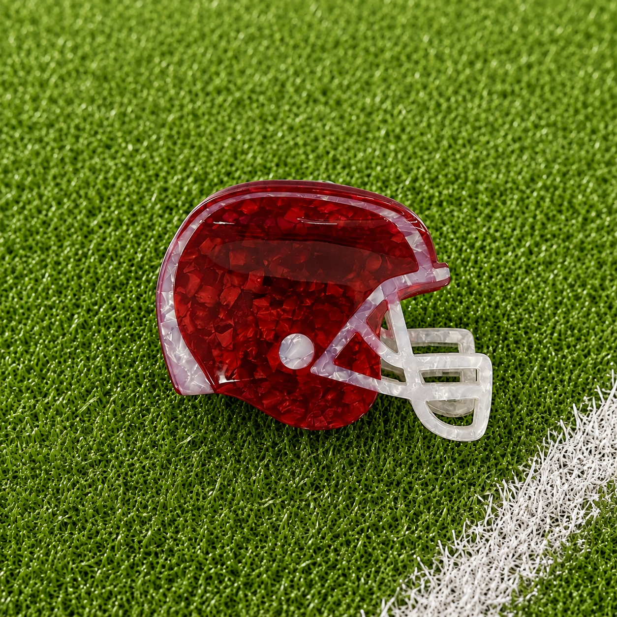 A maroon football helmet shaped claw clip on green turf background