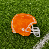 An orange football helmet shaped claw clip on green turf background
